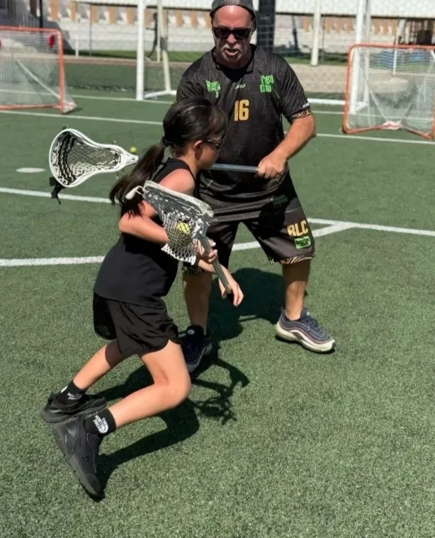 A coach guides a young player through stick work on an outdoor pitch